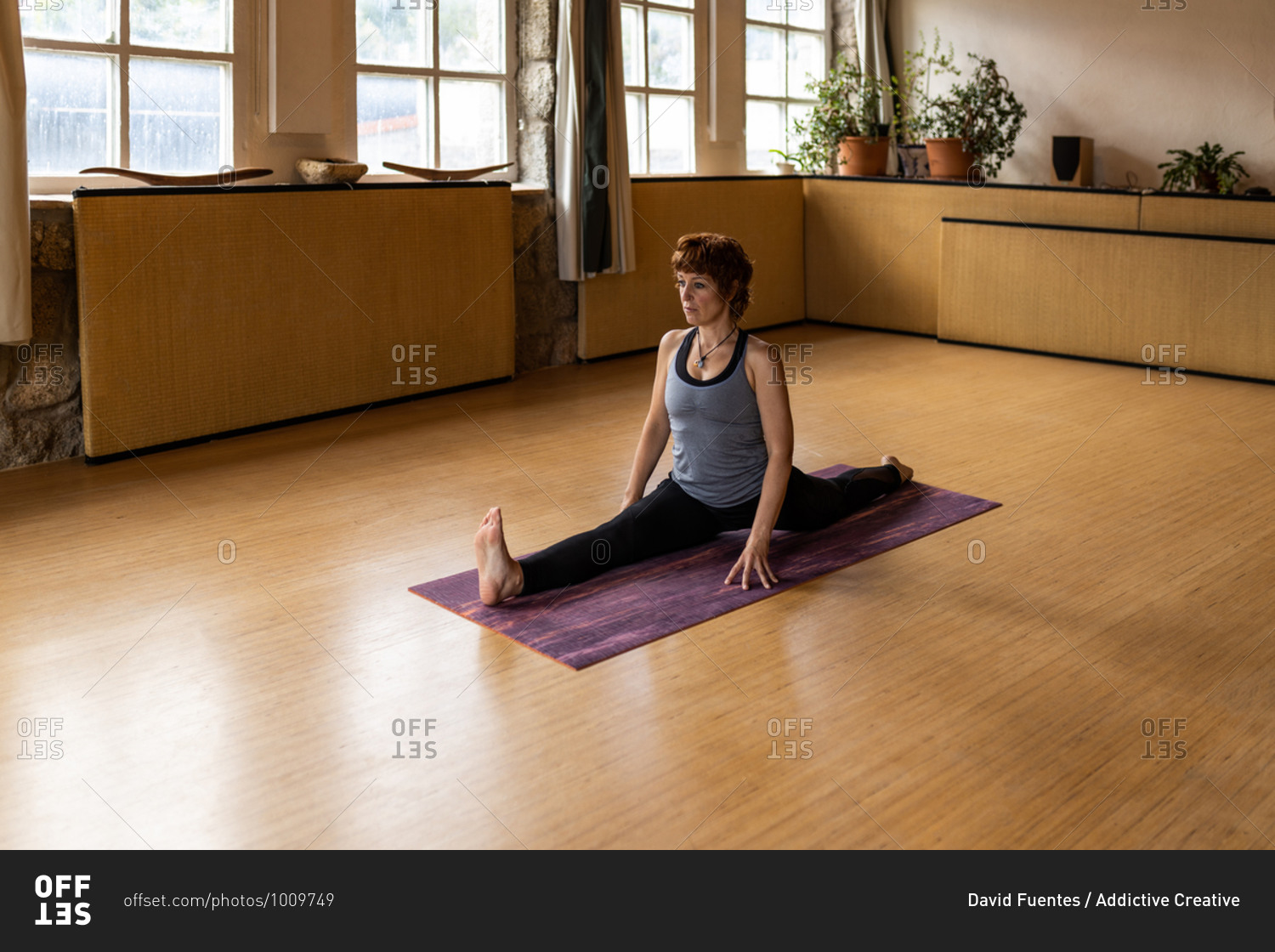 Full body of focused female yogi in sportswear performing monkey pose during Shakti yoga practice in spacious room with wooden interior looking away