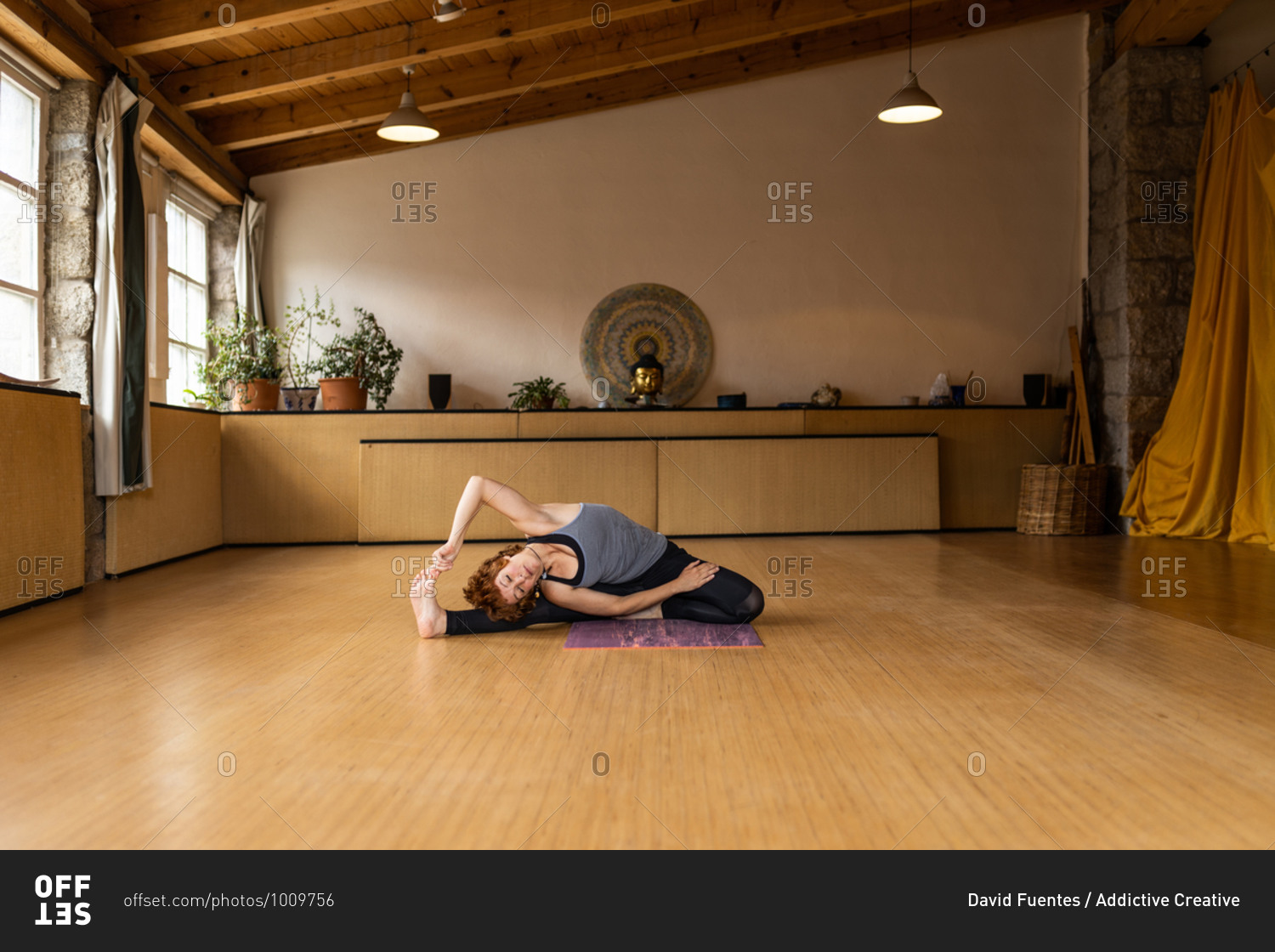 Female in sportswear sitting in revolved seated angle while practicing Shakti yoga alone in light studio with wooden interior in tropical resort