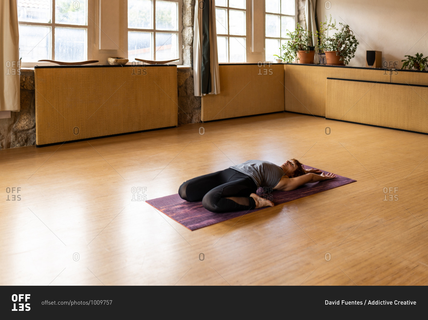 Full body side view of flexible female in sportswear performing Extended Supine Hero pose during Shakti yoga practice in spacious studio with wooden interior