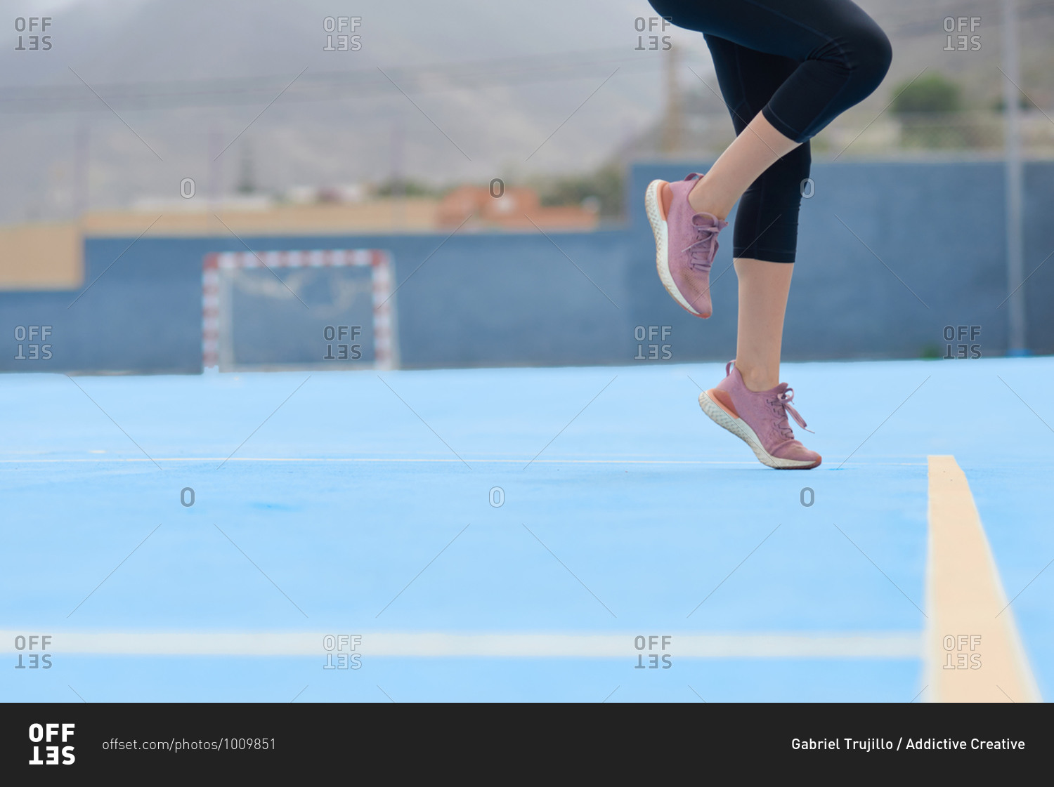Side view of crop active female in sports leggings and sneakers performing jump exercises while warming up before running on sports ground