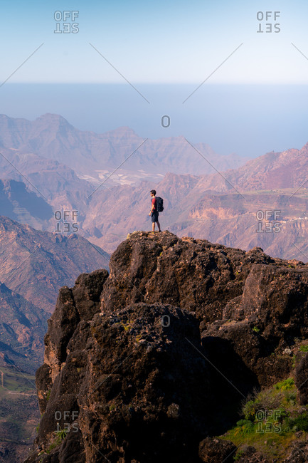 Side view of unrecognizable tourist standing on rough rock and enjoying breathtaking view of highland area in Gran Canaria