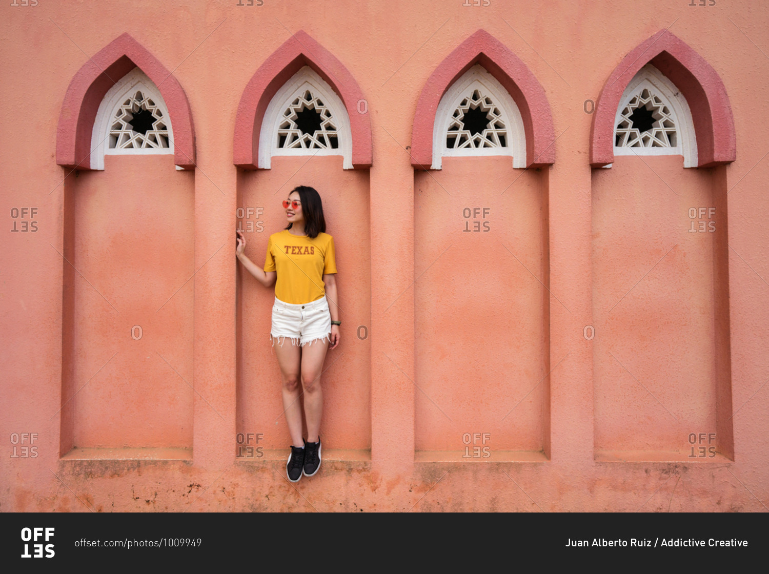 Full length of Asian female traveler standing in arched window of Pink Mosque while sightseeing in Kota Kinabalu during summer holiday and looking away