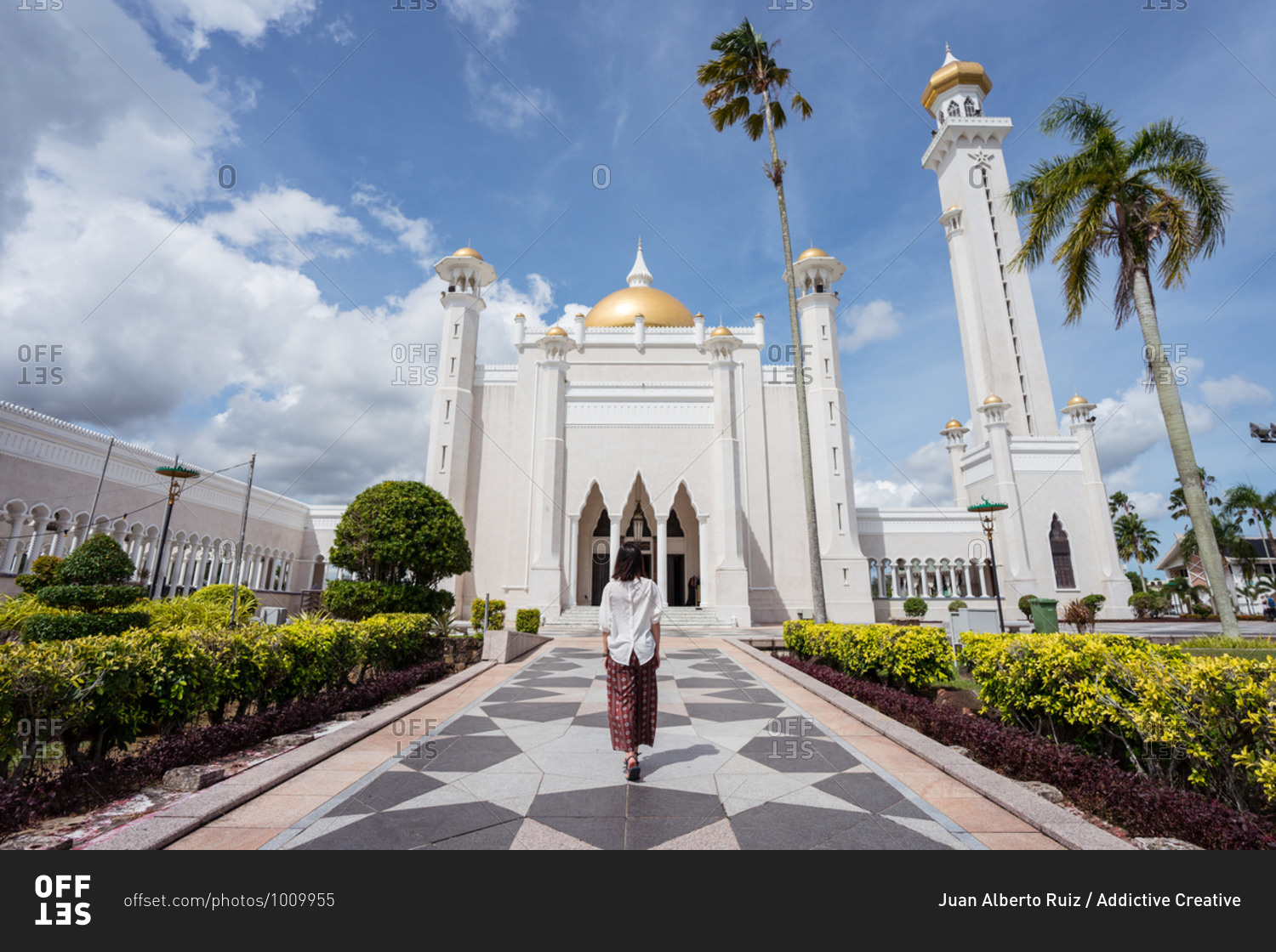 back view of unrecognizable female tourist standing on tiled path in front of Omar Ali Saifuddien Mosque and enjoying summer vacation in Bandar Seri Begawan