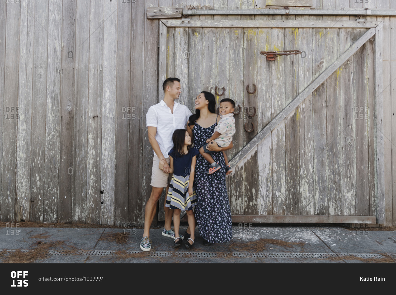 A happy young family standing together in front of an old wooden barn