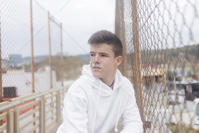 Handsome young guy leaning on a railing outdoors and looking to the side