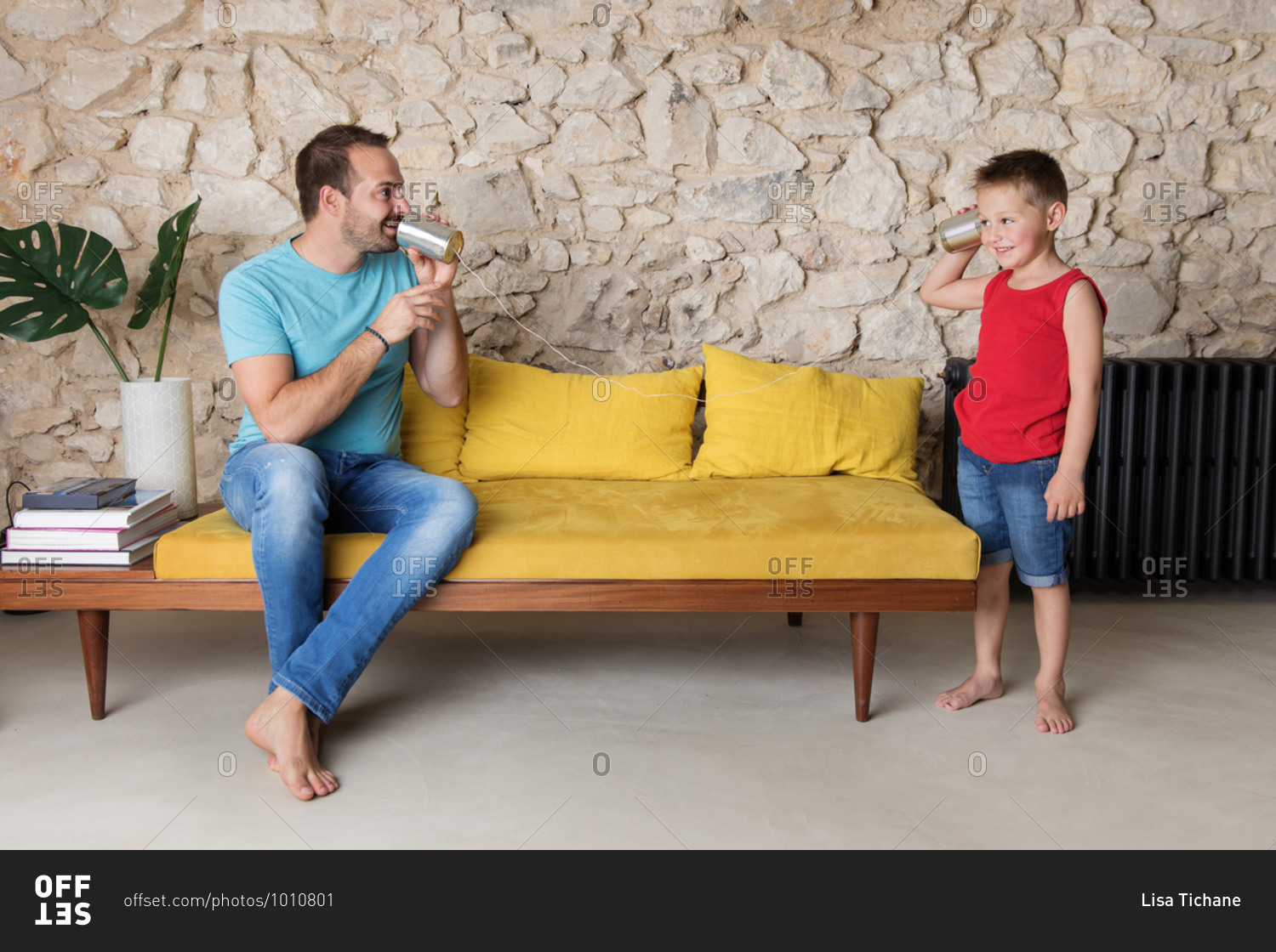 Father and son playing with tin can telephone on yellow sofa