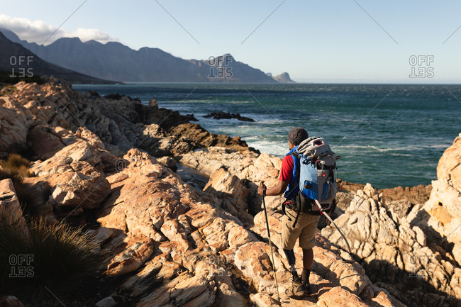 A fit, disabled mixed race male athlete with prosthetic leg, enjoying his time on a trip to the mountains, hiking on the rocks by the sea. Active lifestyle with disability.