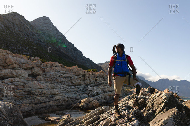 A fit, disabled mixed race male athlete with prosthetic leg, enjoying his time on a trip to the mountains, hiking, admiring the view. Active lifestyle with disability.
