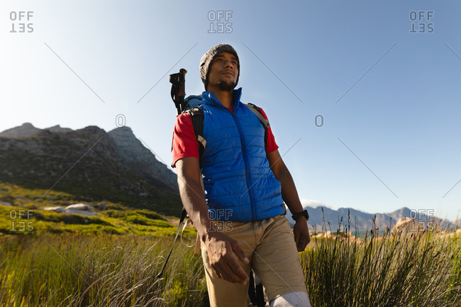 A fit, disabled mixed race male athlete with prosthetic leg, enjoying his time on a trip to the mountains, hiking, walking through grass. Active lifestyle with disability.