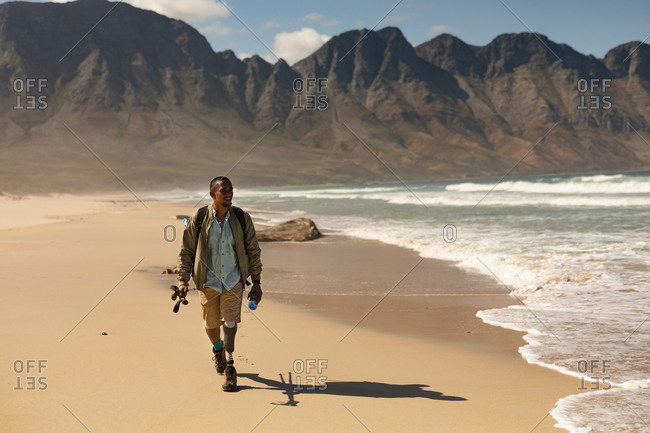 A fit, disabled mixed race male athlete with prosthetic leg, enjoying his time on a trip to the mountains, hiking with sticks, walking on the beach by the sea. Active lifestyle with disability.