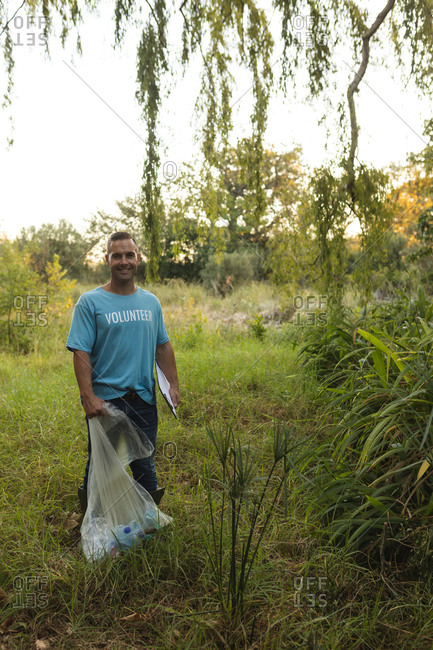 Portrait of happy Caucasian male conservation volunteer cleaning up forest in the countryside, holding clipboard and rubbish bag. Ecology and social responsibility in rural environment.