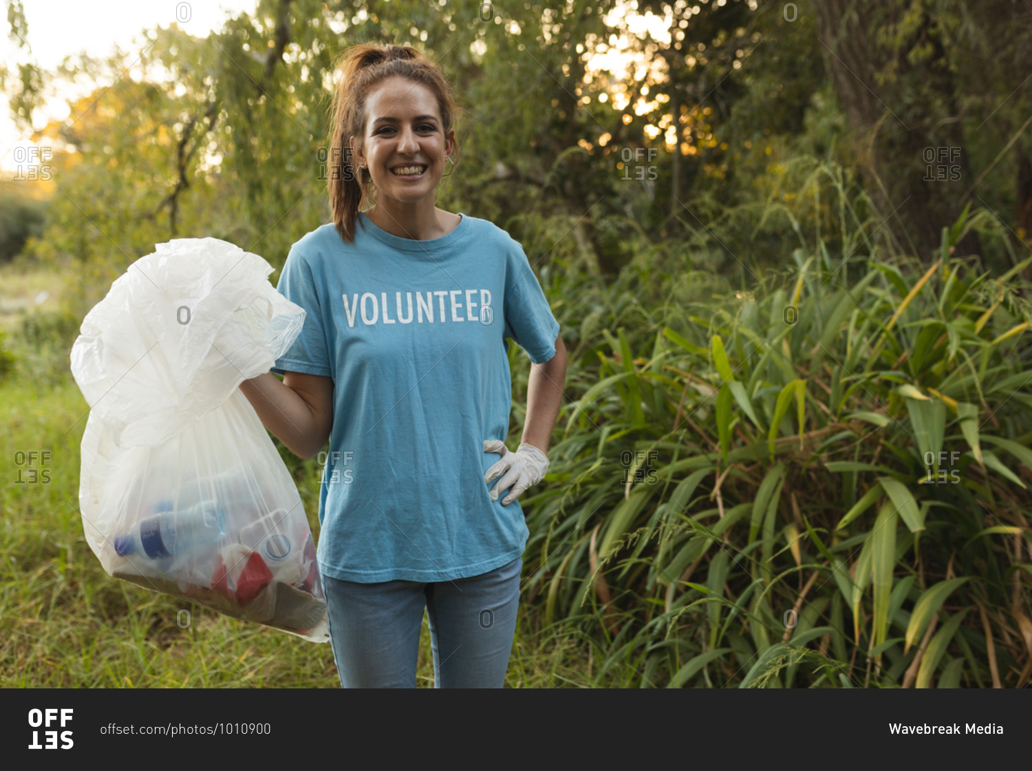 Portrait of happy Caucasian female conservation volunteer cleaning up forest in the countryside, holding rubbish bag, smiling to camera. Ecology and social responsibility in rural environment.