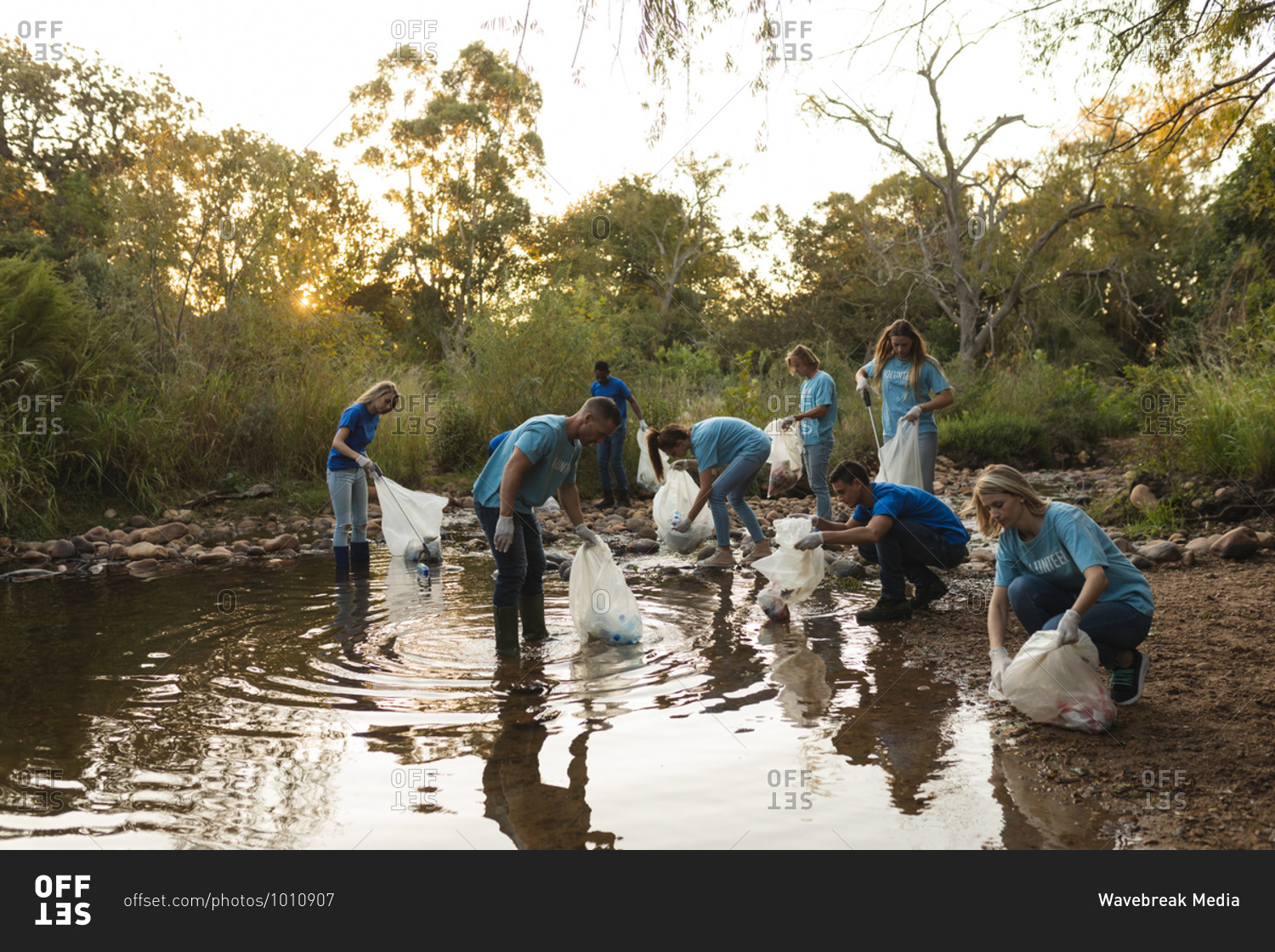 Multi ethnic group of conservation volunteers cleaning up river in the countryside, picking up rubbish. Ecology and social responsibility in rural environment.