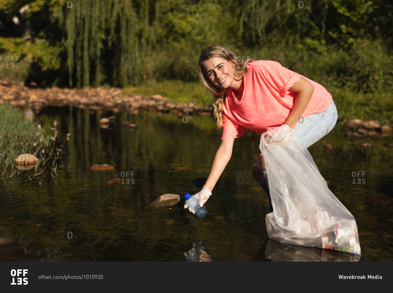 Portrait of Caucasian female conservation volunteer cleaning up river in the countryside, picking up rubbish. Ecology and social responsibility in rural environment.
