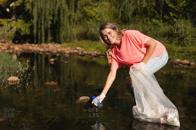 Portrait of Caucasian female conservation volunteer cleaning up river in the countryside, picking up rubbish. Ecology and social responsibility in rural environment.