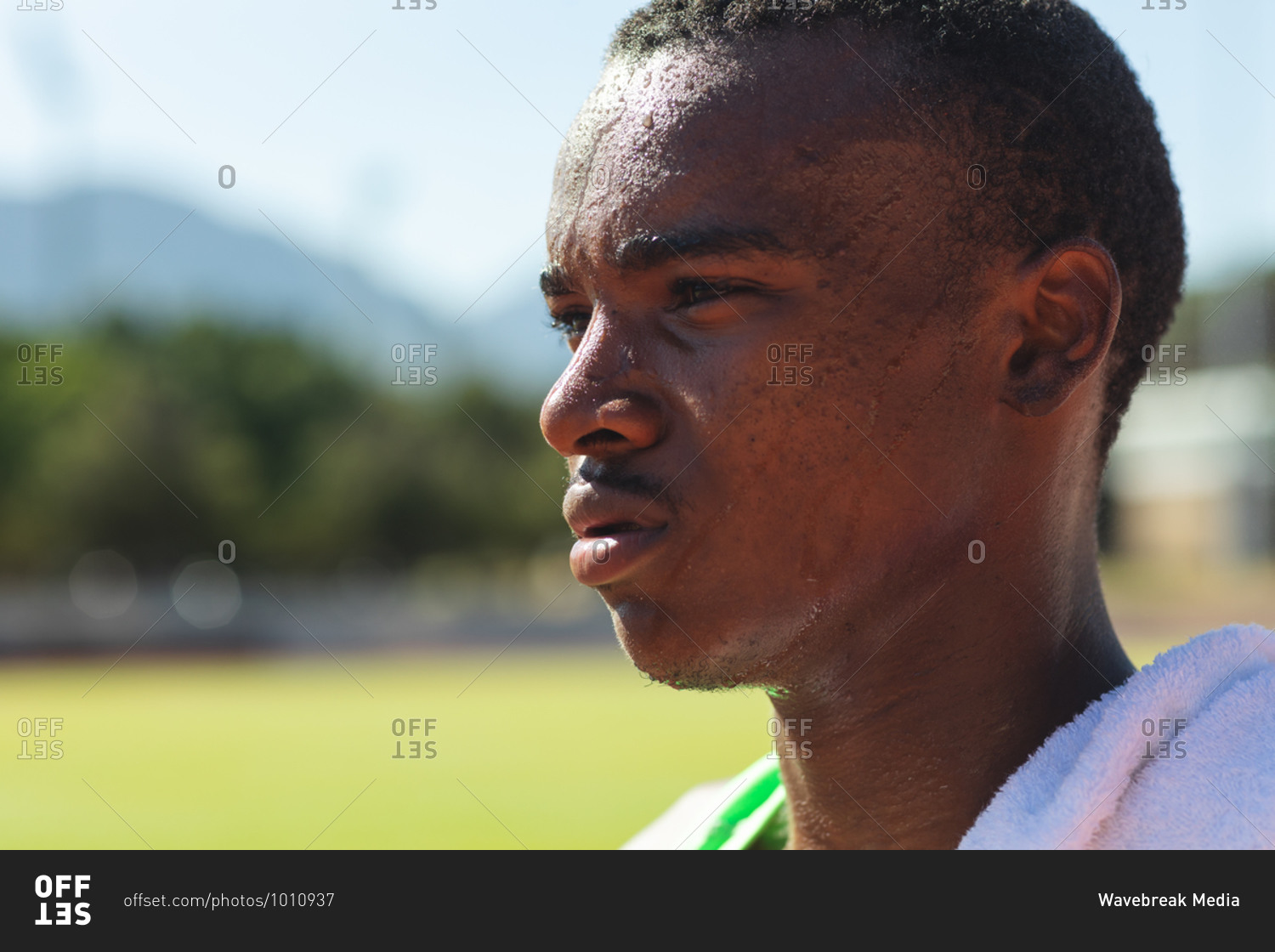 Close up of fit, focused mixed race male athlete at an outdoor sports stadium, on race track after race with towel on his shoulder. Athletics sport training.