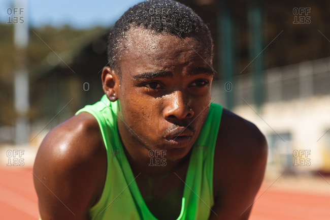 Close up of fit, focused mixed race male athlete at an outdoor sports stadium, on race track after race breathing and resting. Athletics sport training.