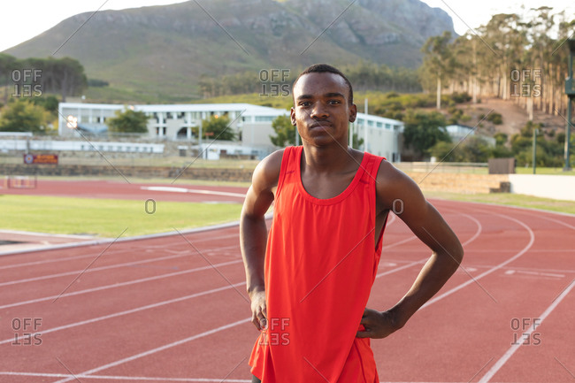 Portrait of fit, focused mixed race male athlete at an outdoor sports stadium, on race track with arms on hips looking at camera. Athletics sport training.