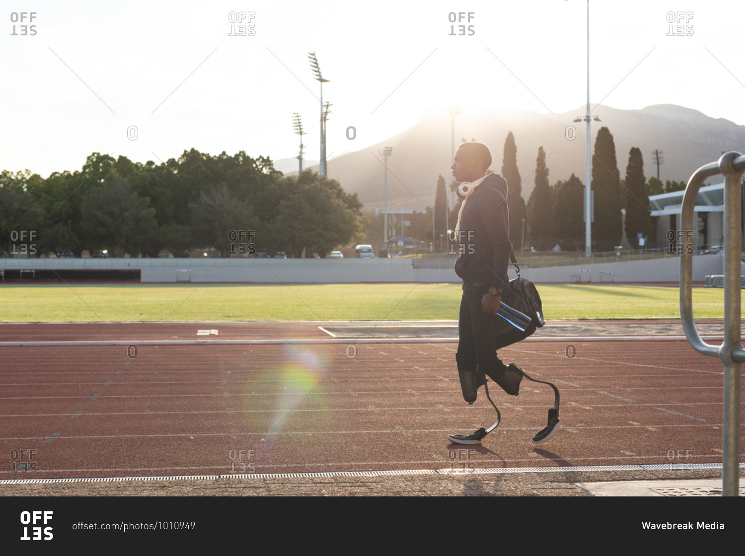 Fit, mixed race disabled male athlete at an outdoor sports stadium, walking with gym bag and water bottle on race track wearing running blades. Disability athletics sport training.