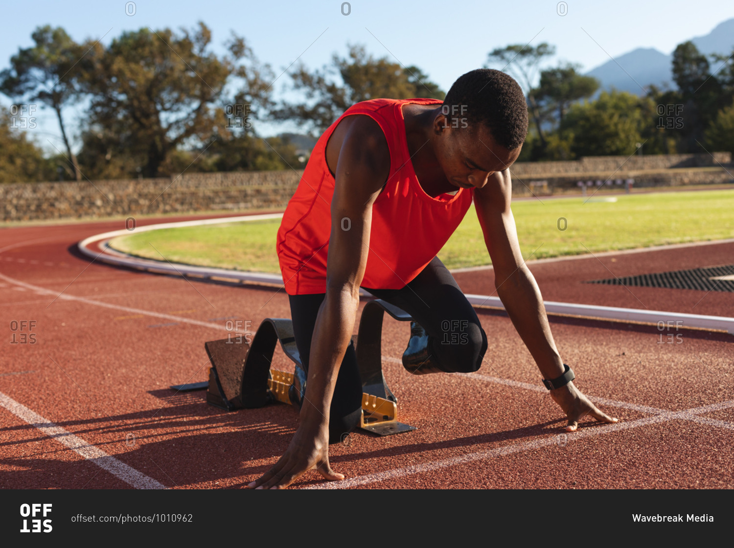 Fit, mixed race disabled male athlete at an outdoor sports stadium, kneeling in  starting blocks on race track wearing running blades. Disability athletics sport training.