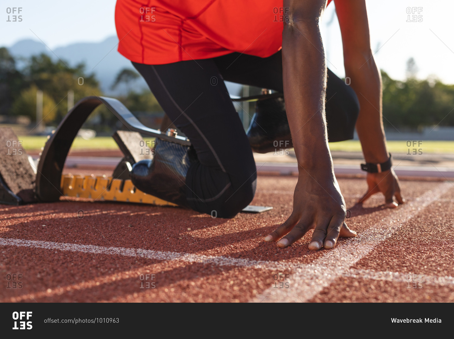 Low section of fit, mixed race disabled male athlete at an outdoor sports stadium, kneeling in starting blocks on race track wearing running blades. Disability athletics sport training.