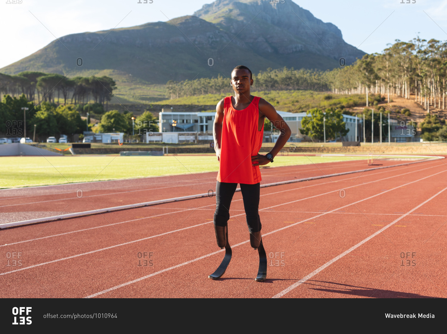 Portrait of fit, mixed race disabled male athlete at an outdoor sports stadium, standing with hands on hips on race track wearing running blades. Disability athletics sport training.