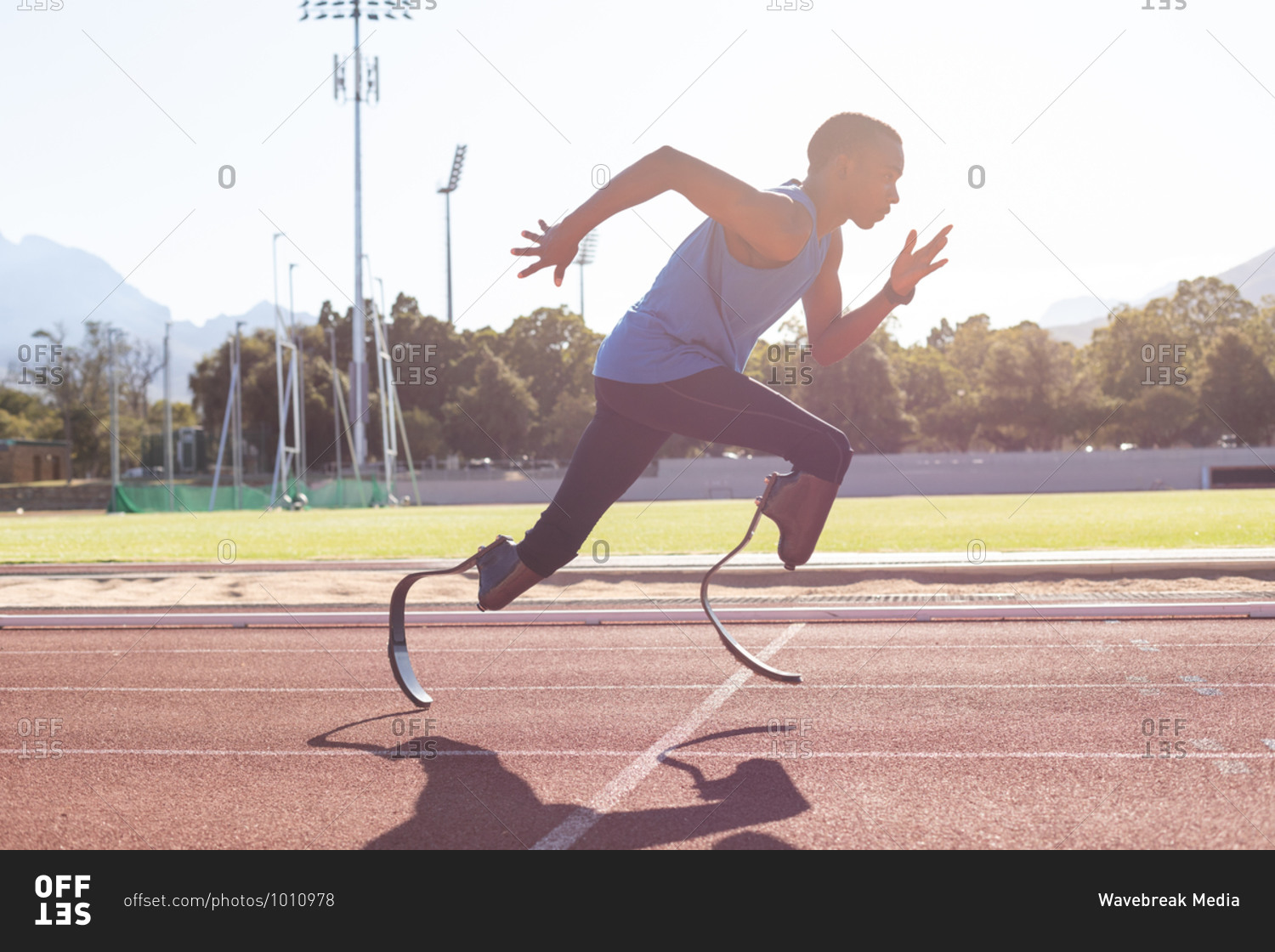 Fit, mixed race disabled male athlete at an outdoor sports stadium, running on race track wearing running blades. Disability athletics sport training.