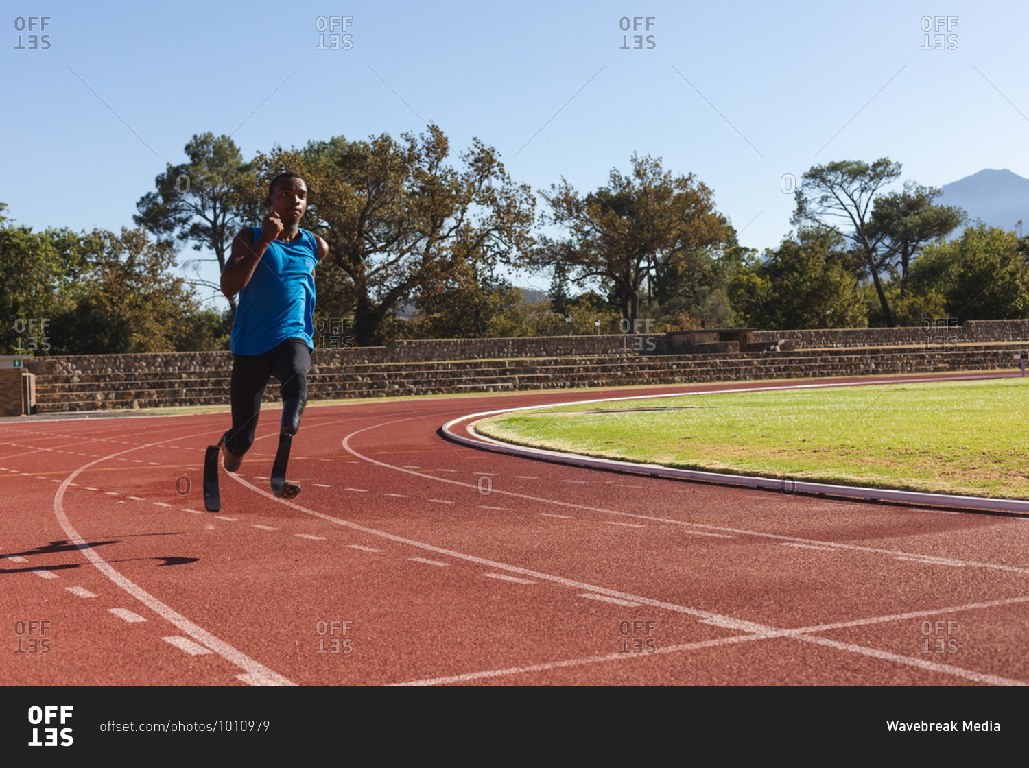 Fit, mixed race disabled male athlete at an outdoor sports stadium, running on race track wearing running blades. Disability athletics sport training.