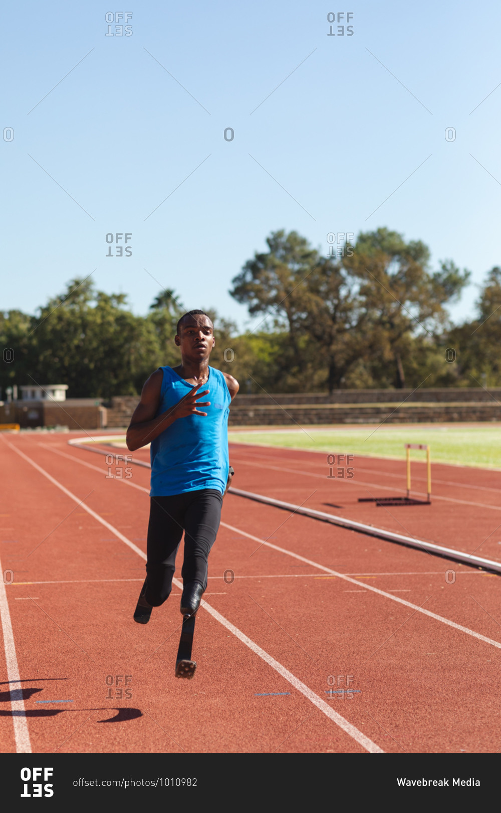 Fit, mixed race disabled male athlete at an outdoor sports stadium, running on race track on running blades. Disability sport training.