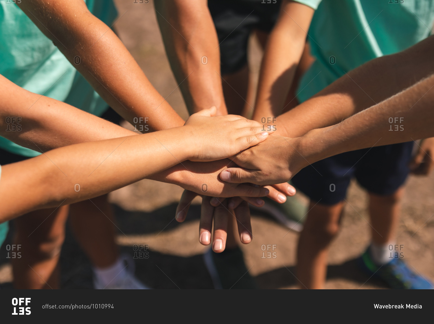 Mid section of a group of Caucasian boys and girls at a boot camp on a sunny day, bonding and stacking hands together before doing an obstacle course, all wearing green t shirts and black shorts