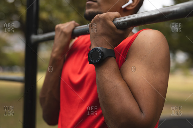 Mid section of mixed race man wearing sportswear, working out in a park in outdoor gym, with wireless earphones and smartwatch, doing pull ups. Fitness strength healthy lifestyle.