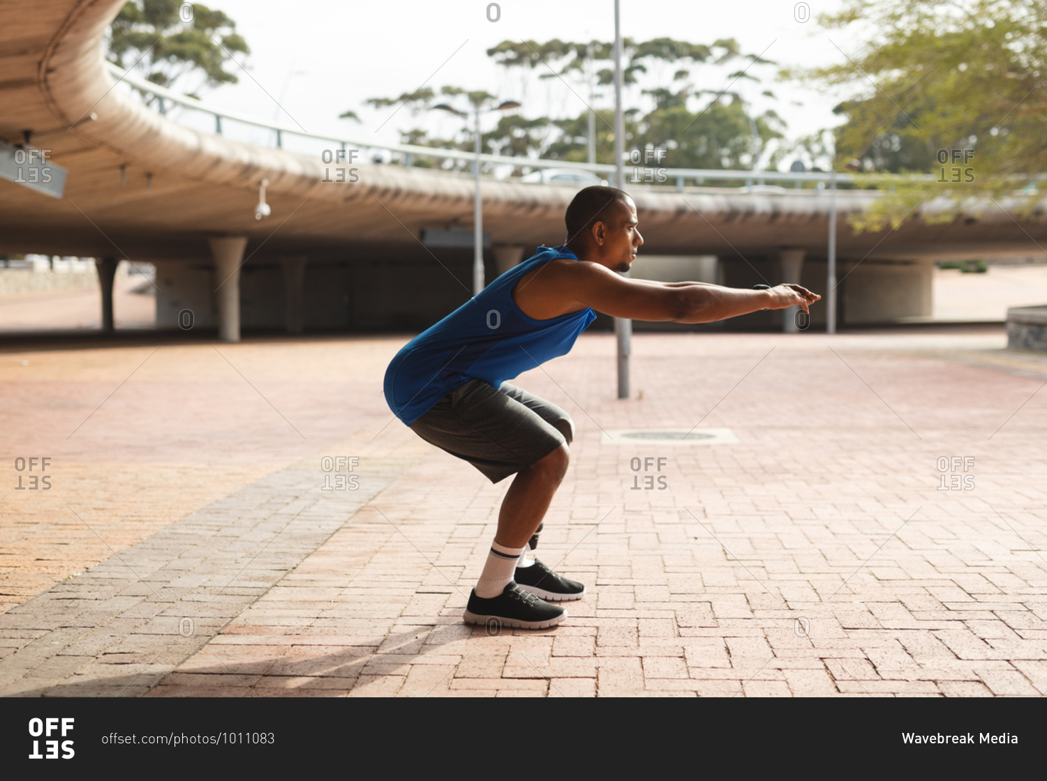 Disabled mixed race man with a prosthetic leg, working out in an urban park, leaning against wall, stretching his leg. Fitness disability healthy lifestyle.