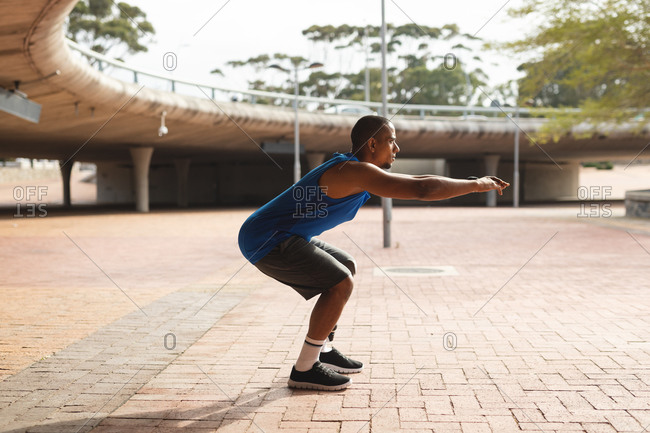 Disabled mixed race man with a prosthetic leg, working out in an urban park, leaning against wall, stretching his leg. Fitness disability healthy lifestyle.