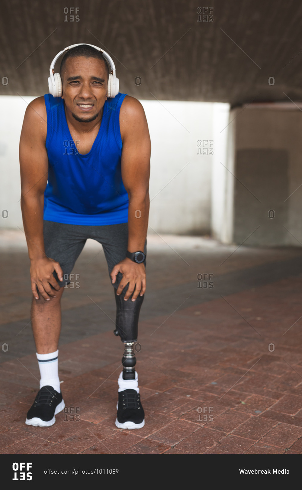Disabled mixed race man with a prosthetic leg, working out in an urban park, wearing wireless headphones taking a break. Fitness disability healthy lifestyle.
