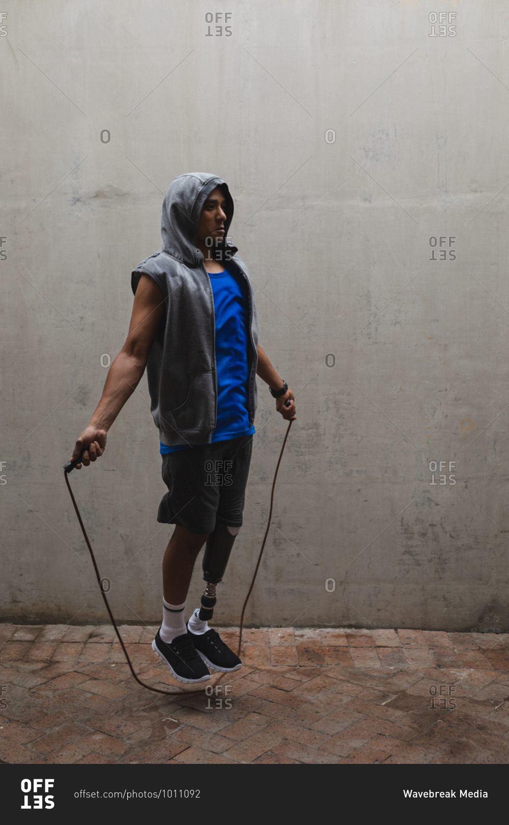 Disabled mixed race man with a prosthetic leg, working out in an urban park, wearing hooded top skipping with skipping rope. Fitness disability healthy lifestyle.