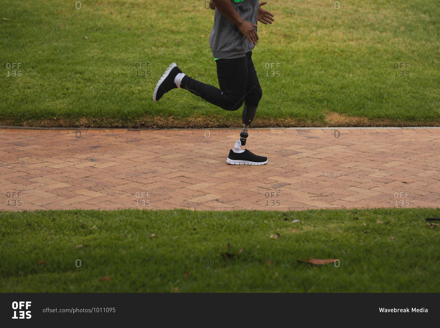 Low section of disabled mixed race man with a prosthetic leg, working out in an urban park, wearing sportswear running on a path. Fitness disability healthy lifestyle.
