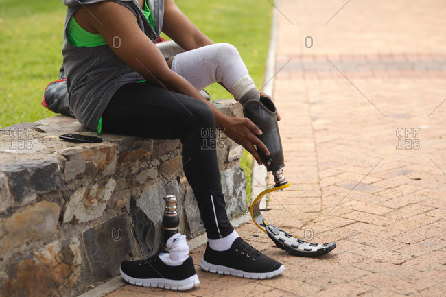 Low section of a disabled mixed race man with a prosthetic leg working out in an urban park, sitting on a wall and fitting a running blade. Fitness disability healthy lifestyle.
