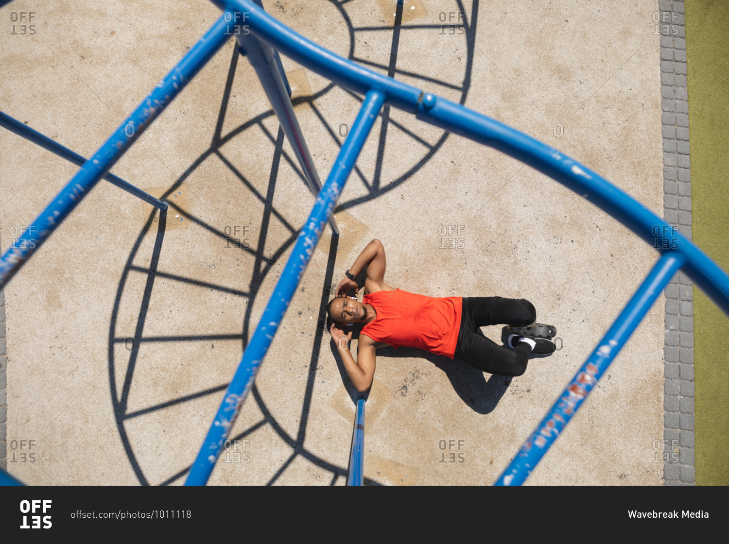 Overhead view of a disabled mixed race man with a prosthetic leg  exercising at an outdoor gym by the coast, doing sit ups in the sun beside the gym equipment. Fitness disability healthy lifestyle.