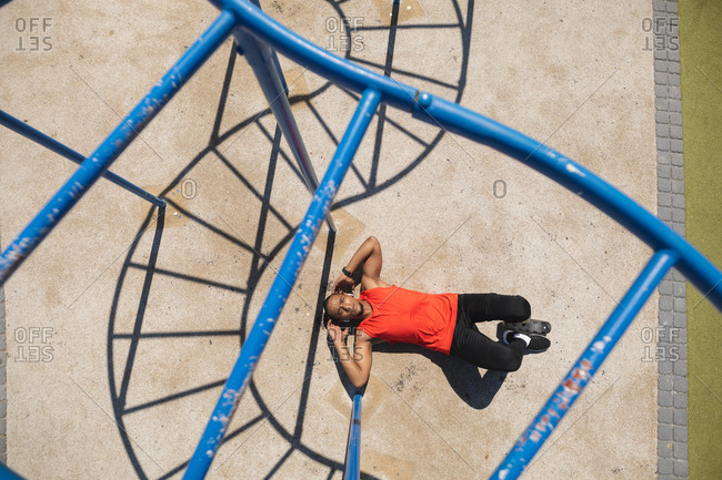 Overhead view of a disabled mixed race man with a prosthetic leg  exercising at an outdoor gym by the coast, doing sit ups in the sun beside the gym equipment. Fitness disability healthy lifestyle.
