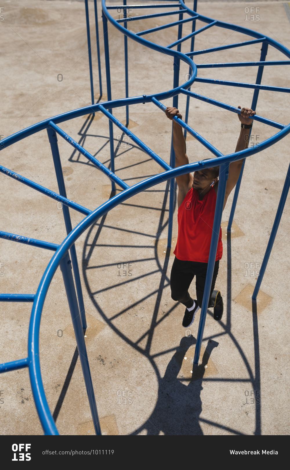 Disabled mixed race man with a prosthetic running blade exercising at an outdoor gym by the coast, wearing wireless earphones, working out on the monkey bars. Fitness disability healthy lifestyle.