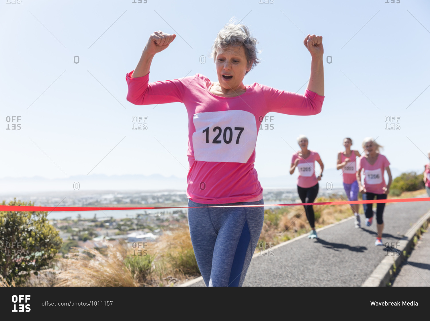 Group of Caucasian female friends enjoying exercising on a sunny day, having running race and wearing numbers, running towards a finish line and celebrating.