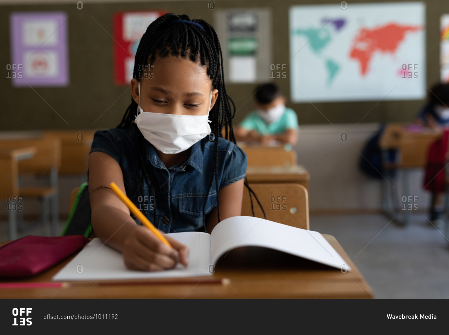 Mixed race girl sitting at desks wearing face mask in classroom. Primary education social distancing health safety during Covid19 Coronavirus pandemic.
