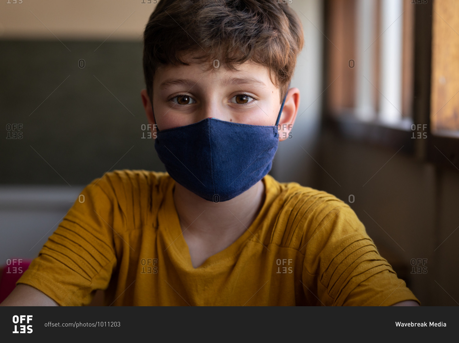 Portrait of a Caucasian boy sitting at desk wearing face mask in classroom. Primary education social distancing health safety during Covid19 Coronavirus pandemic.