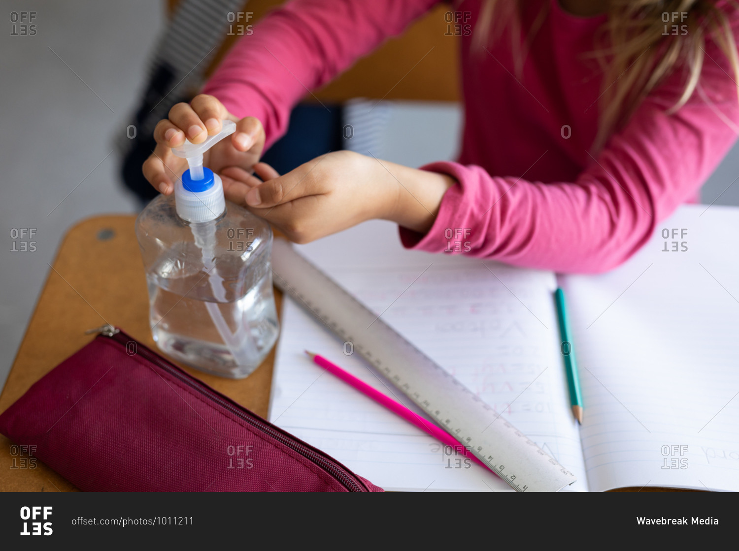 Mid section of a Caucasian girl sitting at desk and sanitizing her hands. Primary education social distancing health safety during Covid19 Coronavirus pandemic.