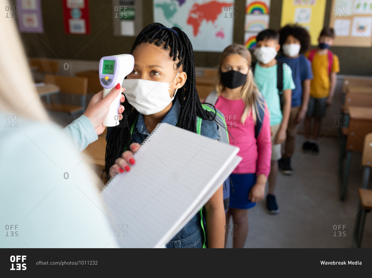 Caucasian female teacher measuring temperature of children in an elementary school. Primary education social distancing health safety during Covid19 Coronavirus pandemic.