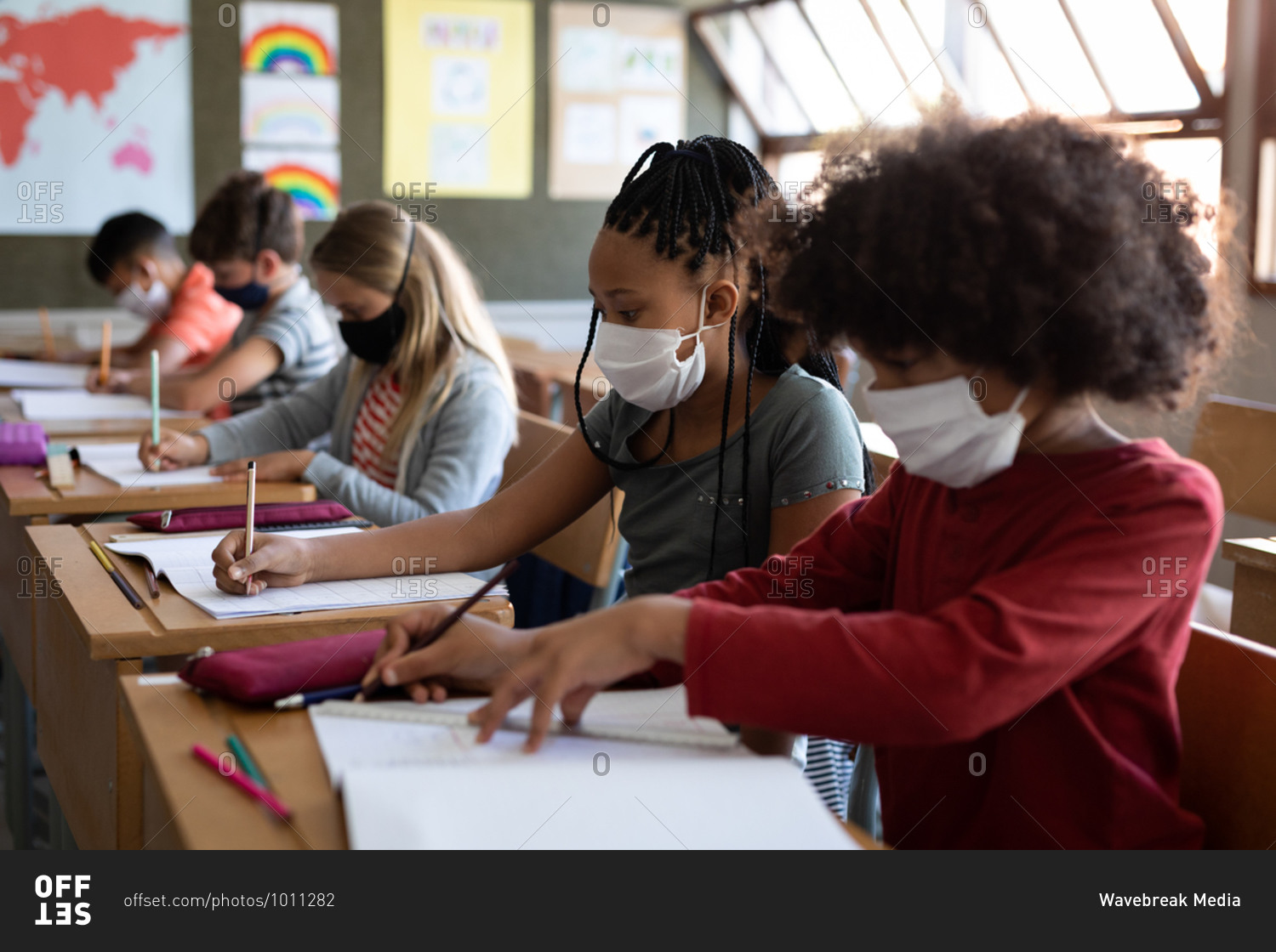 Group of multi ethnic kids wearing face masks while studying in classroom at school. Primary education social distancing health safety during Covid19 Coronavirus pandemic.