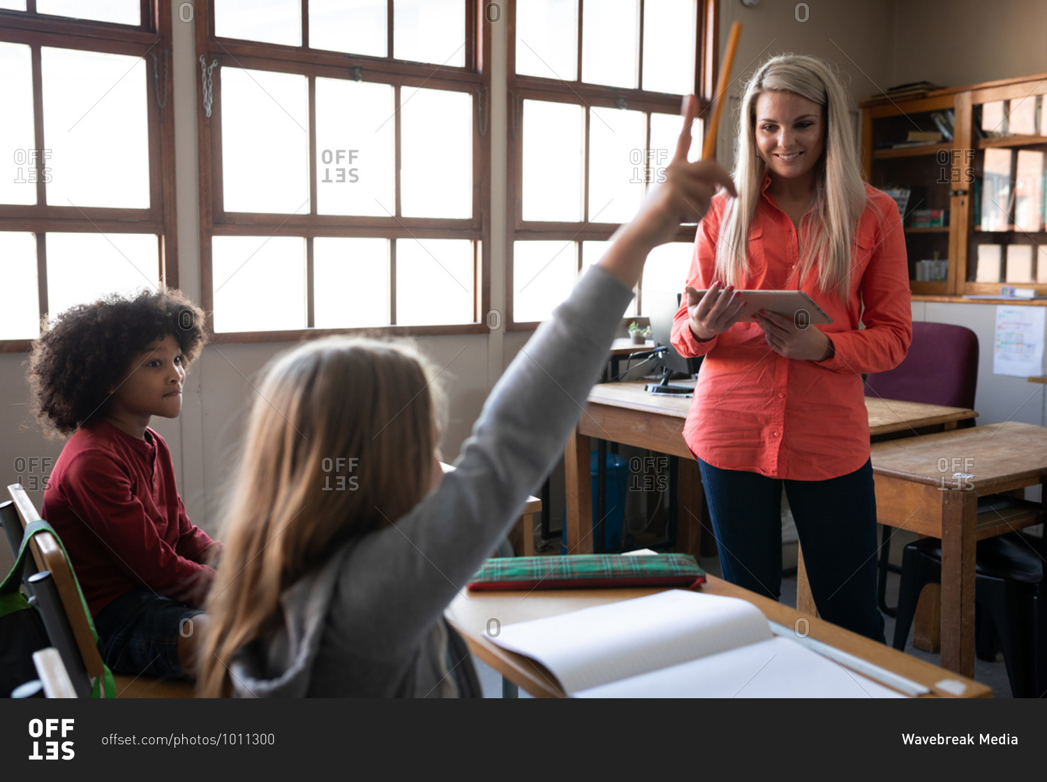 Caucasian girl raising her hand while sitting on her desk during the lesson with Caucasian female teacher.  Primary education social distancing health safety during Covid19 Coronavirus pandemic.