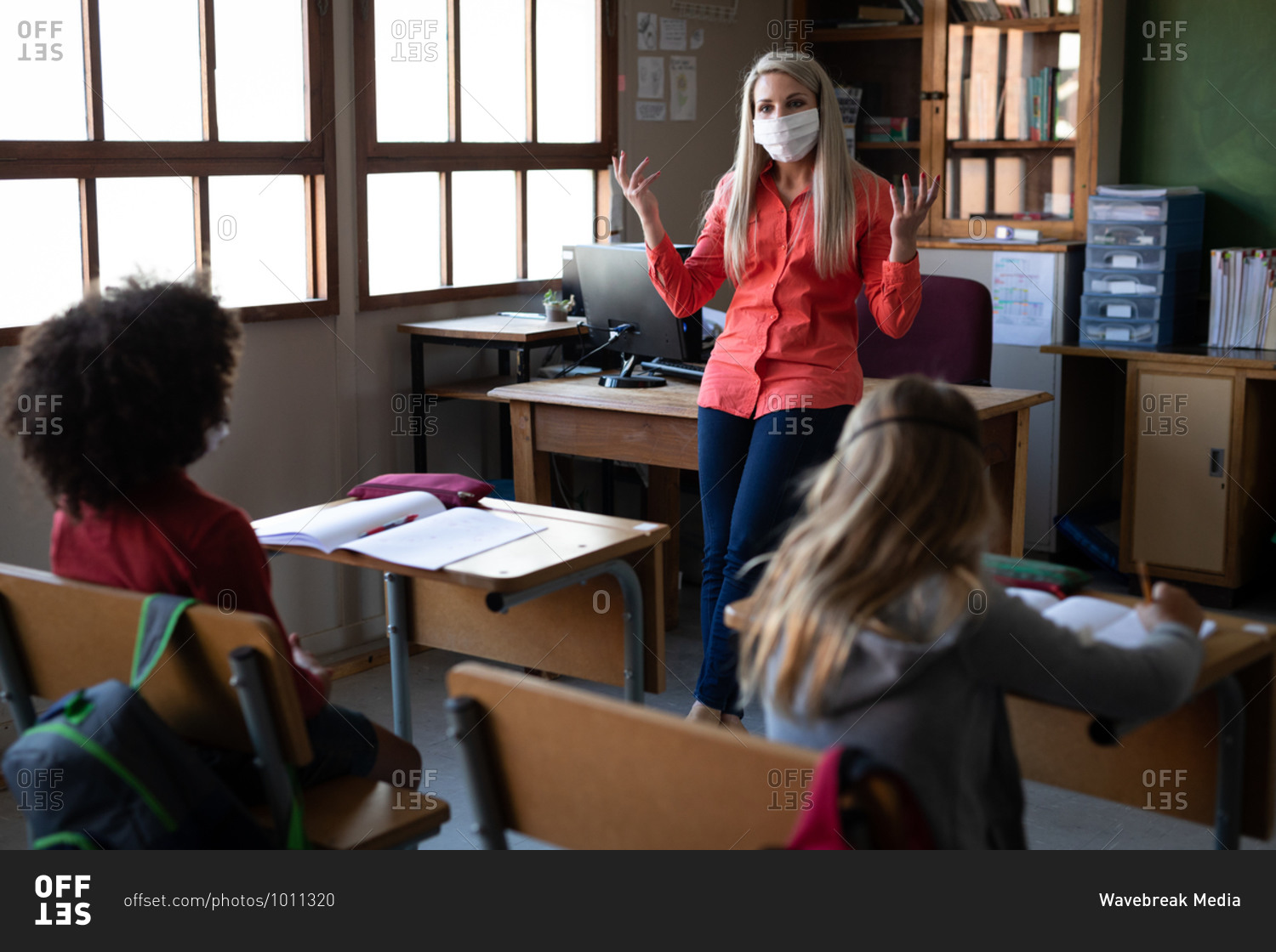 Female Caucasian teacher wearing face mask teaching in class at school. Primary education social distancing health safety during Covid19 Coronavirus pandemic.