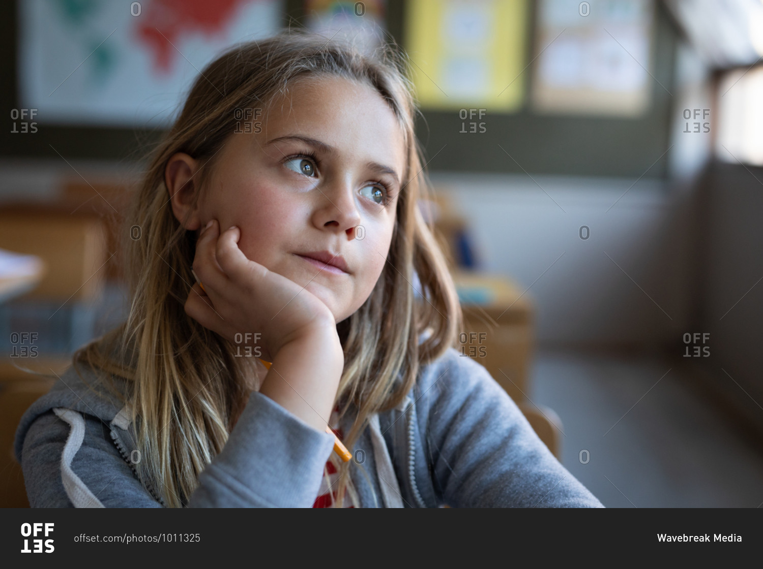 Thoughtful Caucasian girl sitting on her desk at school. Primary education social distancing health safety during Covid19 Coronavirus pandemic.