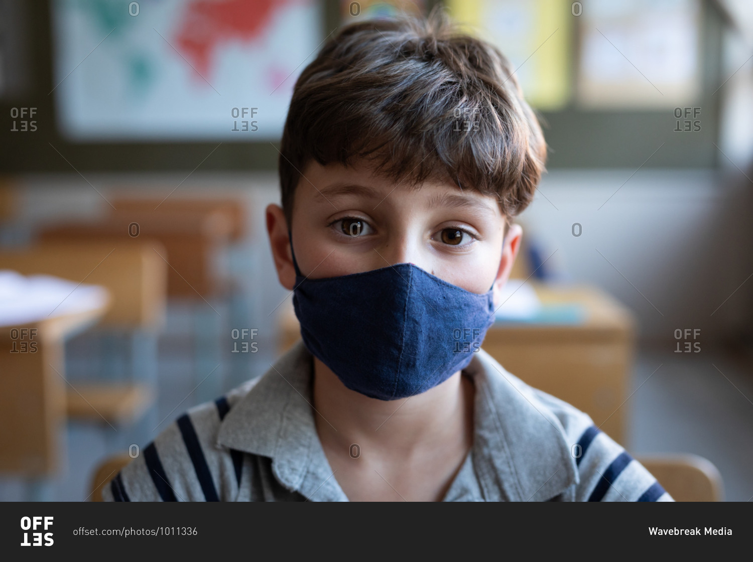 Portrait of a Caucasian boy wearing a face mask, sitting on his desk in class at school. Primary education social distancing health safety during Covid19 Coronavirus pandemic.